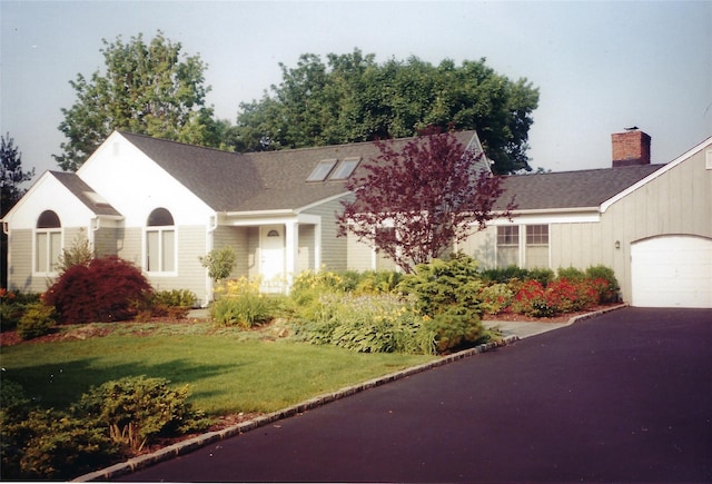 ranch-style house featuring driveway, roof with shingles, a front yard, an attached garage, and a chimney