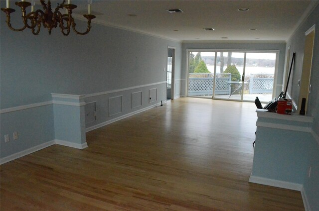 empty room with a notable chandelier, crown molding, and wood finished floors