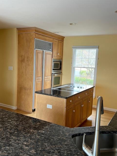 kitchen featuring built in appliances, brown cabinetry, a sink, and dark stone counters