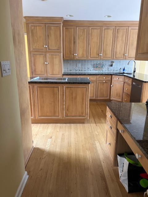 kitchen with backsplash, a sink, dishwashing machine, brown cabinetry, and dark stone counters