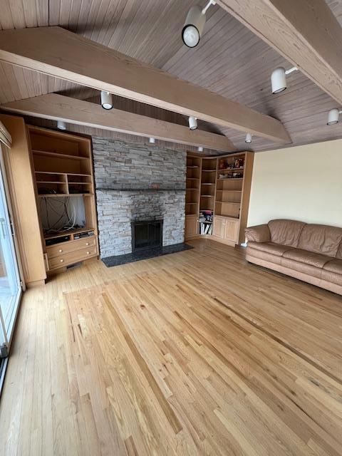 unfurnished living room with wood ceiling, vaulted ceiling with beams, wood finished floors, a stone fireplace, and built in features
