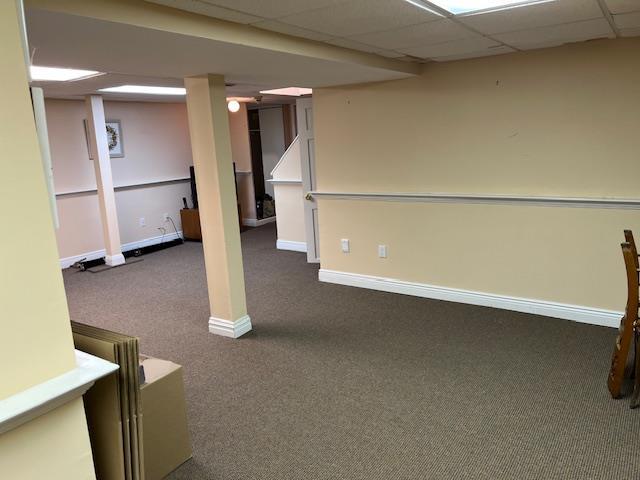 finished basement featuring baseboards, dark carpet, and a paneled ceiling