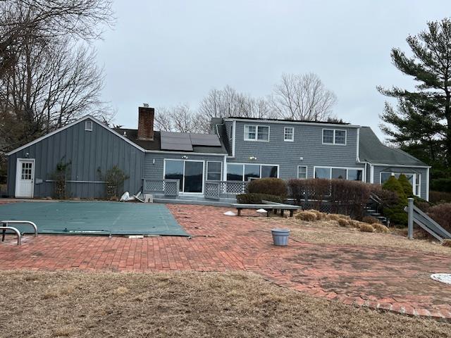 rear view of house with a patio, a chimney, board and batten siding, and solar panels