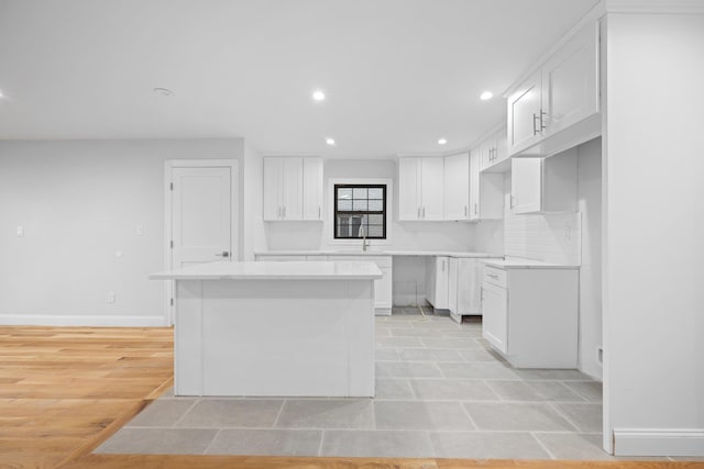 kitchen with white cabinetry, a center island, sink, and light hardwood / wood-style flooring