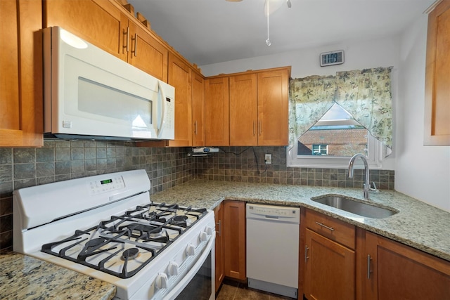 kitchen with brown cabinets, tasteful backsplash, a sink, light stone countertops, and white appliances