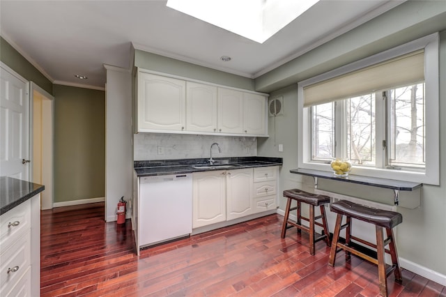 kitchen featuring a skylight, decorative backsplash, dishwasher, ornamental molding, and a sink