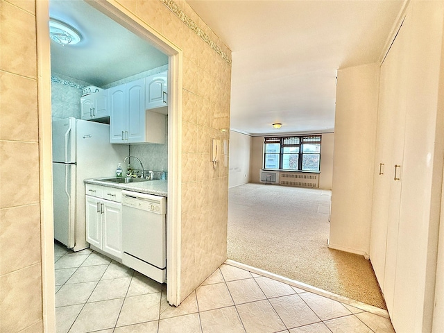 kitchen featuring sink, light carpet, radiator heating unit, white appliances, and white cabinets