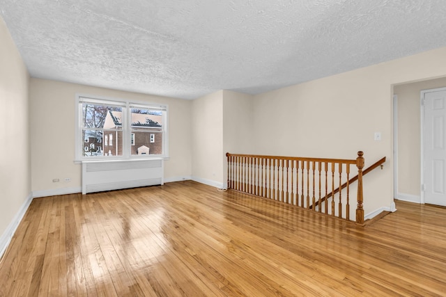 spare room featuring radiator heating unit, a textured ceiling, and light wood-type flooring