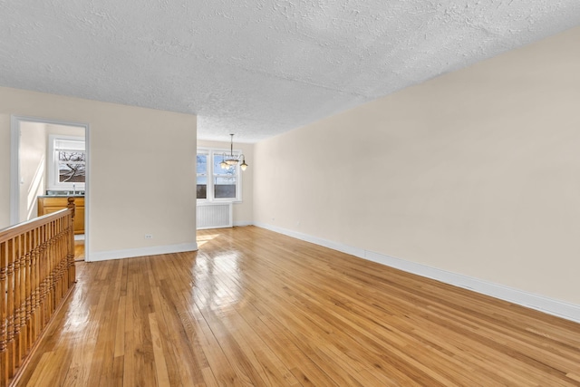 empty room with sink, an inviting chandelier, radiator heating unit, a textured ceiling, and light wood-type flooring