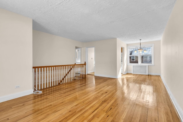 unfurnished living room with radiator heating unit, a chandelier, light hardwood / wood-style flooring, and a textured ceiling