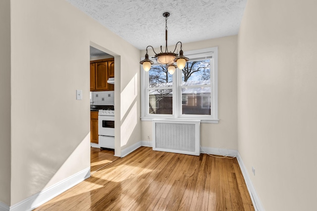 unfurnished dining area featuring a notable chandelier, radiator, a textured ceiling, and light wood-type flooring