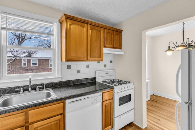 kitchen with pendant lighting, sink, light wood-type flooring, backsplash, and white appliances