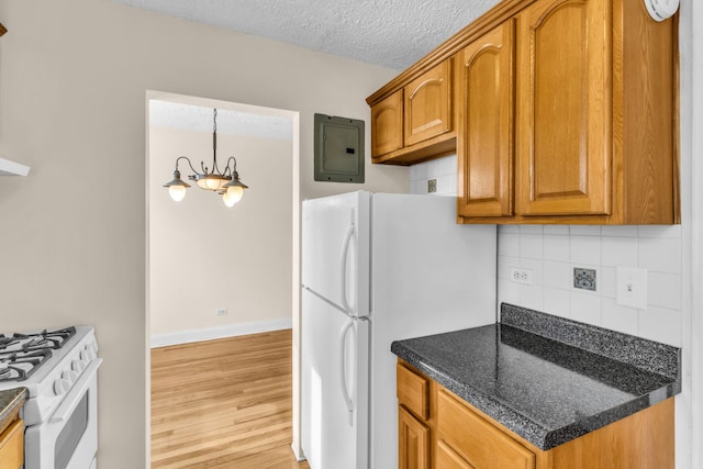 kitchen with a textured ceiling, dark stone countertops, light hardwood / wood-style flooring, white appliances, and backsplash