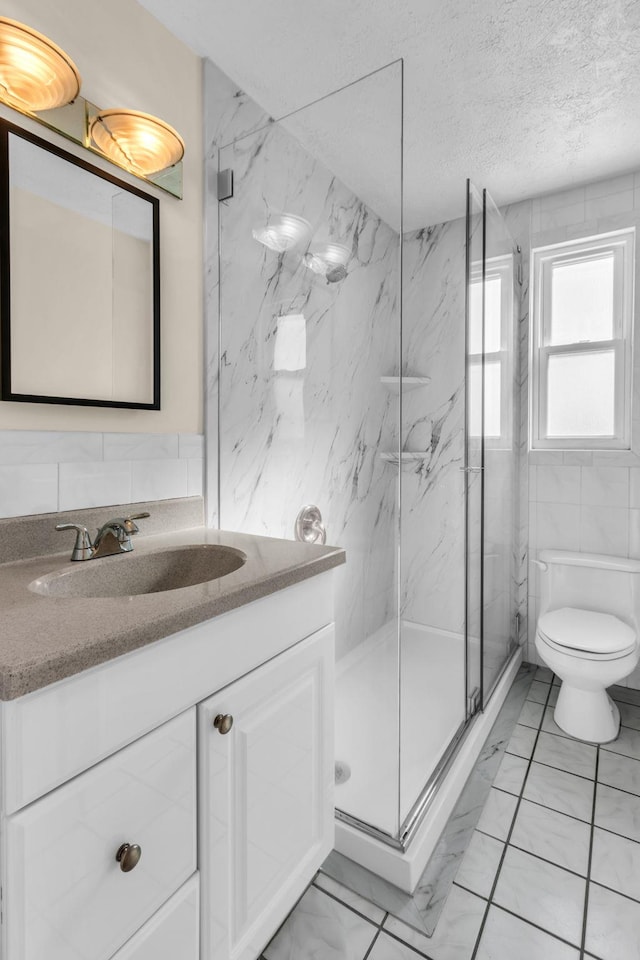 bathroom with tile walls, vanity, an enclosed shower, a textured ceiling, and toilet