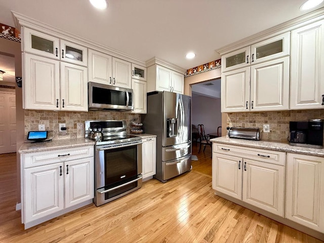 kitchen featuring appliances with stainless steel finishes, backsplash, light stone counters, white cabinets, and light wood-type flooring