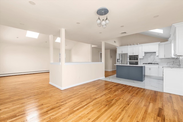 kitchen featuring appliances with stainless steel finishes, decorative backsplash, white cabinets, a kitchen island, and decorative light fixtures