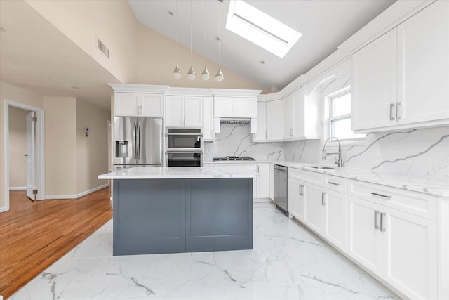 kitchen featuring a center island, stainless steel appliances, white cabinets, a sink, and light stone countertops