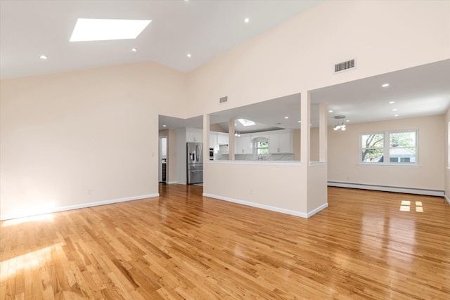 unfurnished living room featuring visible vents, a skylight, high vaulted ceiling, a baseboard heating unit, and light wood finished floors