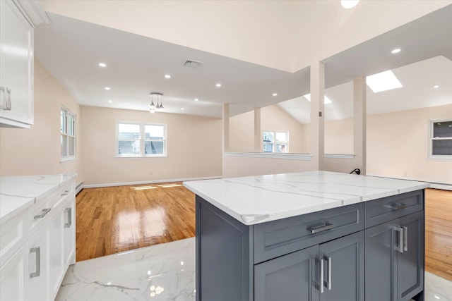 kitchen with white cabinetry, light stone countertops, open floor plan, and light wood-style floors
