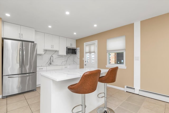 kitchen with a breakfast bar area, baseboard heating, a sink, light tile patterned floors, and stainless steel appliances