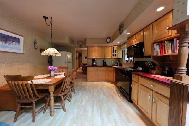 kitchen with dark countertops, light wood-style flooring, glass insert cabinets, black appliances, and wallpapered walls