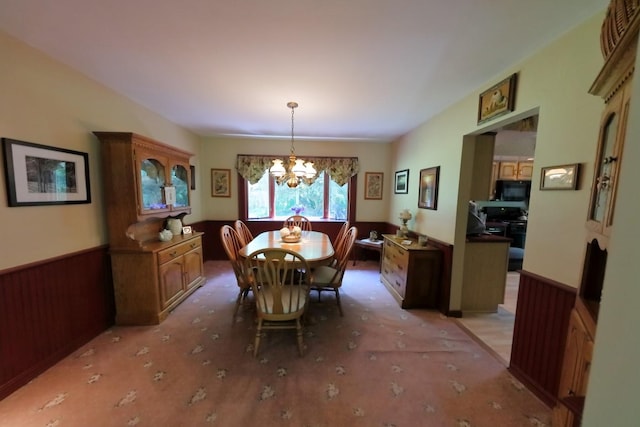 dining area featuring a wainscoted wall, wood walls, and an inviting chandelier