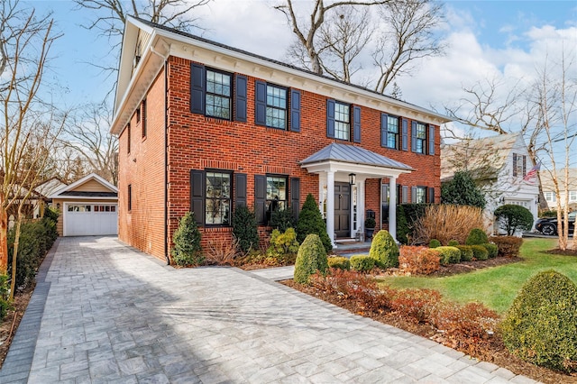 view of front facade with brick siding, a detached garage, and an outbuilding