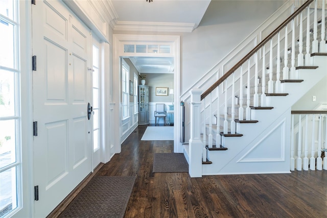 foyer featuring crown molding, dark wood finished floors, a decorative wall, and stairway