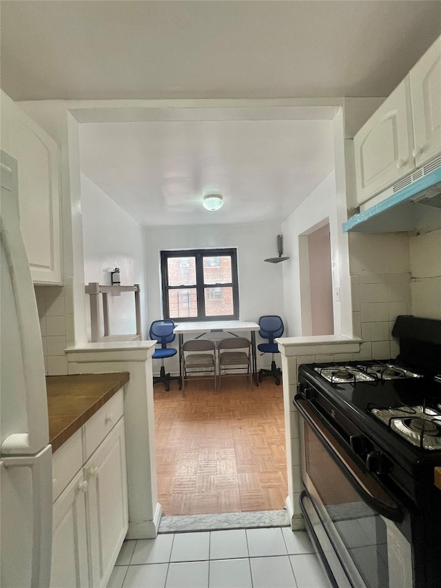 kitchen with black gas range, white cabinetry, tasteful backsplash, and light parquet floors