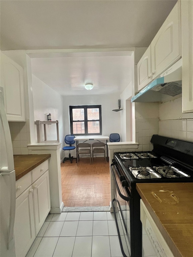 kitchen featuring white cabinetry, tasteful backsplash, light tile patterned floors, black gas range oven, and white fridge