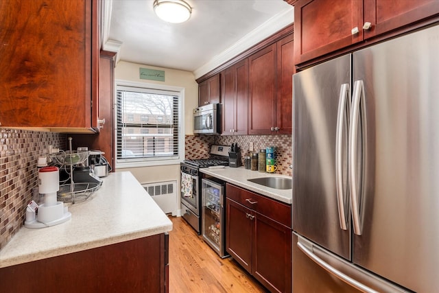 kitchen with appliances with stainless steel finishes, radiator heating unit, wine cooler, tasteful backsplash, and light hardwood / wood-style floors