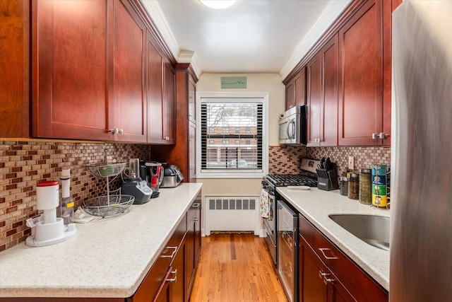 kitchen with light stone counters, appliances with stainless steel finishes, radiator, light hardwood / wood-style floors, and decorative backsplash