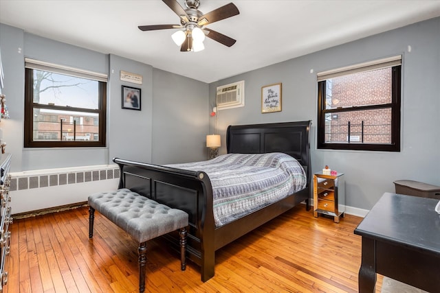 bedroom featuring ceiling fan, radiator heating unit, light hardwood / wood-style floors, and an AC wall unit