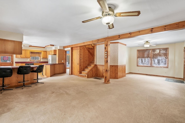 carpeted living room featuring ceiling fan, wooden walls, and beamed ceiling