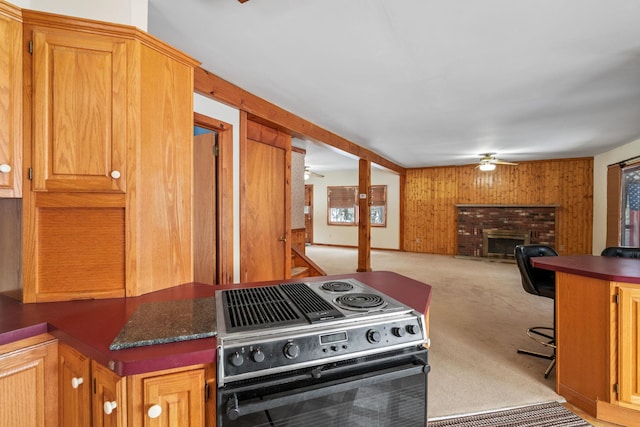 kitchen featuring electric range oven, wooden walls, a fireplace, ceiling fan, and light carpet