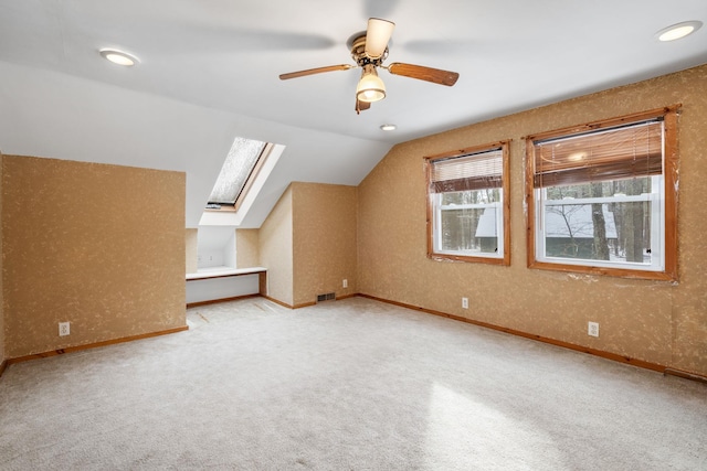 additional living space featuring ceiling fan, vaulted ceiling with skylight, and light carpet