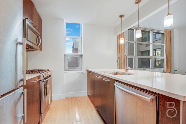 kitchen featuring appliances with stainless steel finishes, sink, pendant lighting, and light wood-type flooring