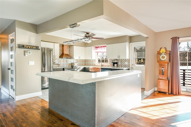 kitchen featuring white cabinetry, stainless steel refrigerator, hardwood / wood-style floors, and wall chimney range hood