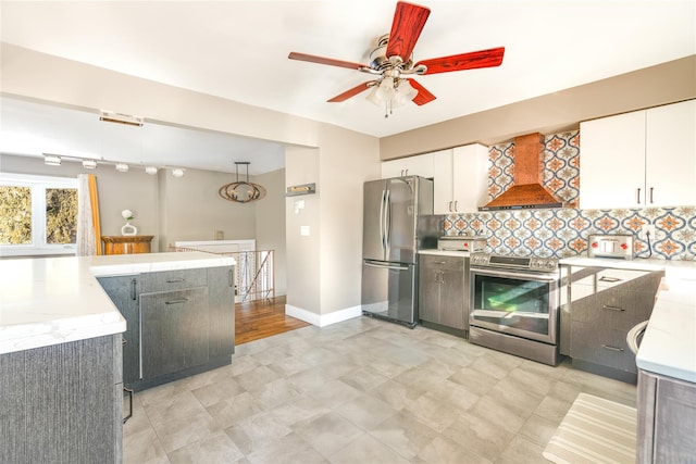 kitchen featuring appliances with stainless steel finishes, light stone counters, custom range hood, white cabinets, and decorative backsplash