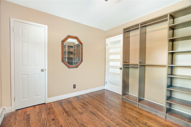 unfurnished bedroom with dark hardwood / wood-style floors and a baseboard heating unit