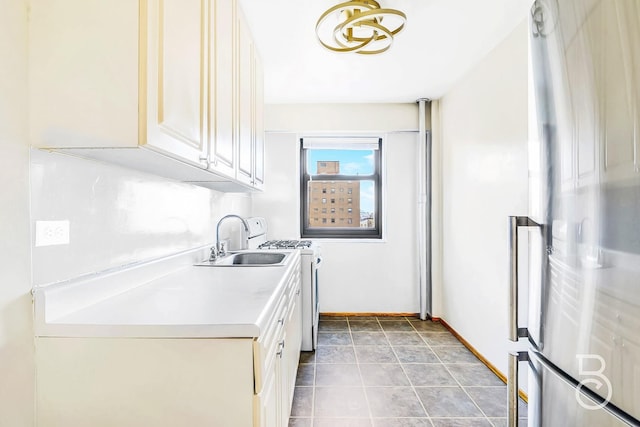 kitchen featuring sink, backsplash, white range with gas cooktop, tile patterned flooring, and stainless steel refrigerator