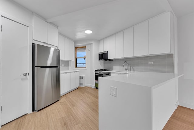 kitchen with appliances with stainless steel finishes, tasteful backsplash, sink, white cabinets, and light hardwood / wood-style flooring