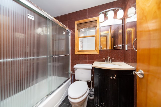 full bathroom featuring tile walls, backsplash, bath / shower combo with glass door, vanity, and toilet