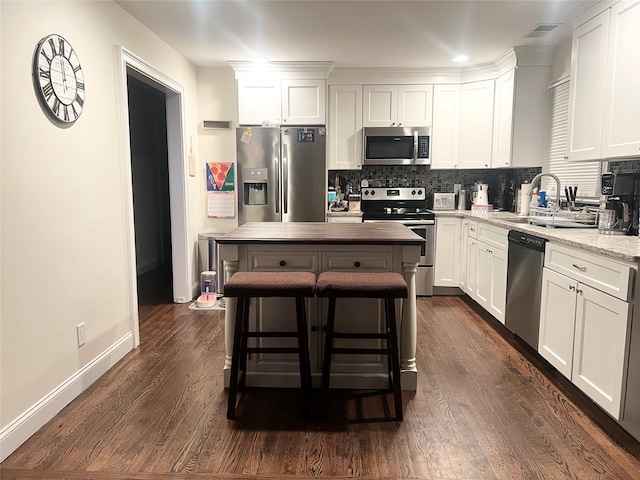 kitchen with visible vents, light stone counters, stainless steel appliances, white cabinetry, and backsplash