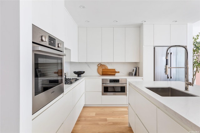 kitchen with appliances with stainless steel finishes, sink, white cabinets, and light hardwood / wood-style flooring