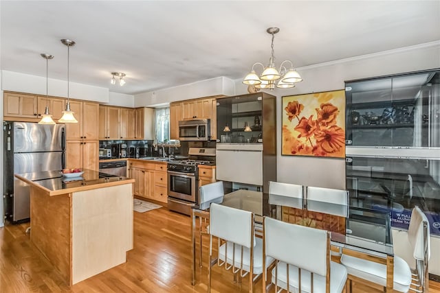 kitchen with sink, an inviting chandelier, hanging light fixtures, stainless steel appliances, and light hardwood / wood-style floors