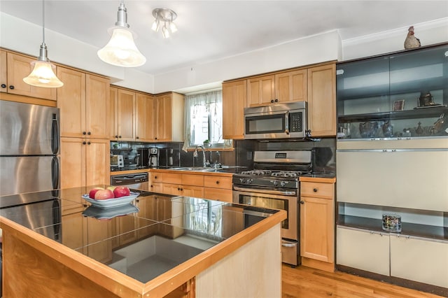 kitchen with pendant lighting, tasteful backsplash, sink, stainless steel appliances, and light hardwood / wood-style flooring