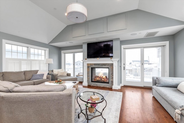 living room with lofted ceiling, visible vents, wood finished floors, and a multi sided fireplace