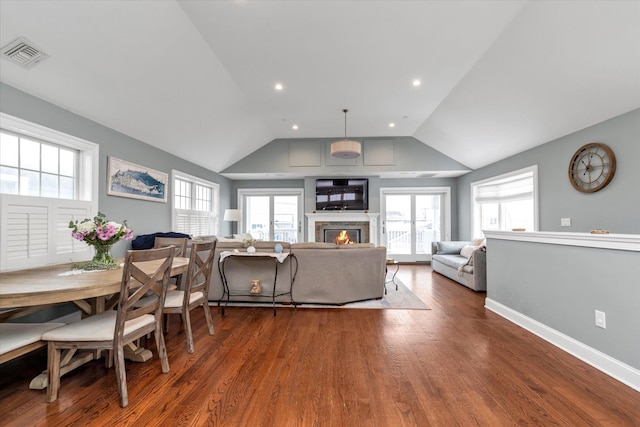 living area with dark wood-style flooring, visible vents, a glass covered fireplace, vaulted ceiling, and baseboards