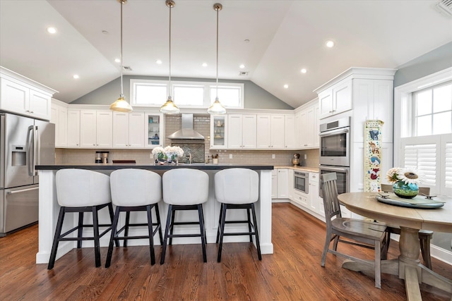 kitchen with pendant lighting, appliances with stainless steel finishes, white cabinets, a kitchen island, and wall chimney exhaust hood